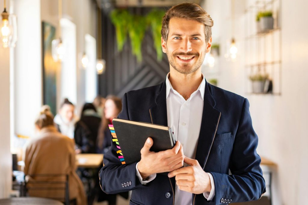 a man in blue suit smiling while holding his notebook